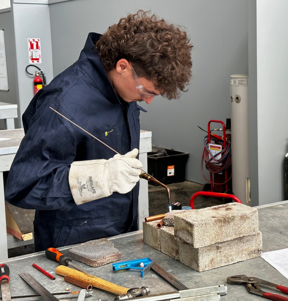 A gasfitting apprentice brazing copper pipe during hands-on training
